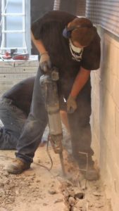 Worker jackhammering basement floor to create a trench