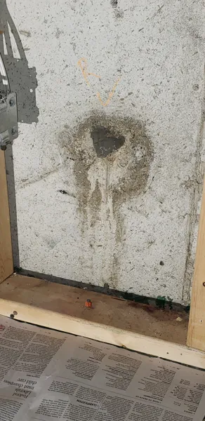 Water dripping from a small round tie-rod hole in a basement foundation wall.