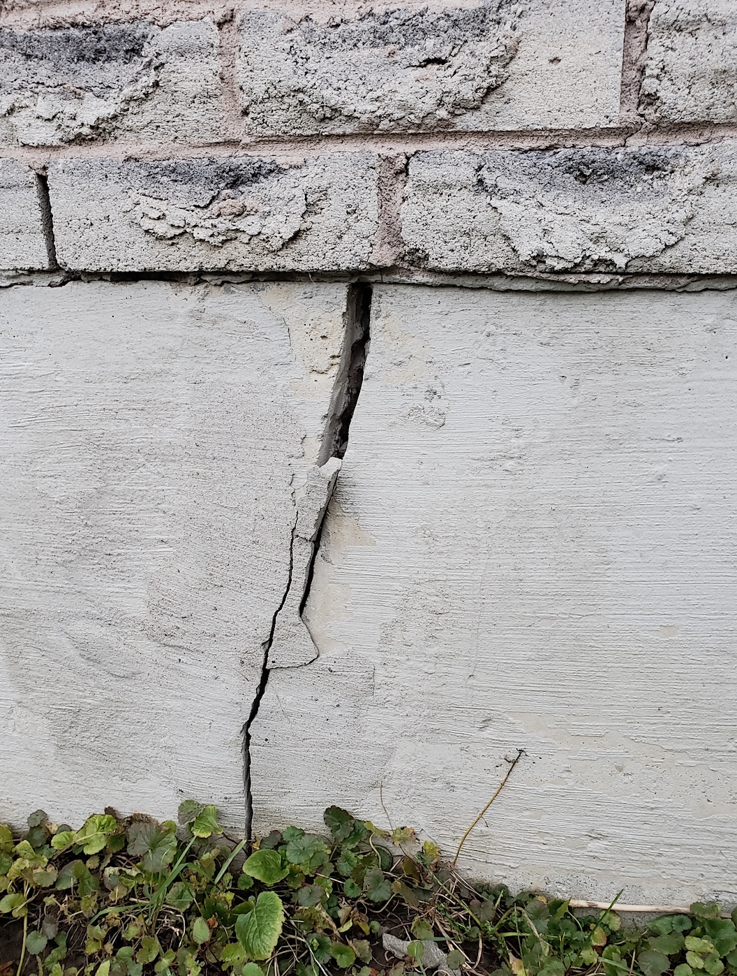 Large vertical crack visible on exterior concrete foundation wall beneath brick veneer