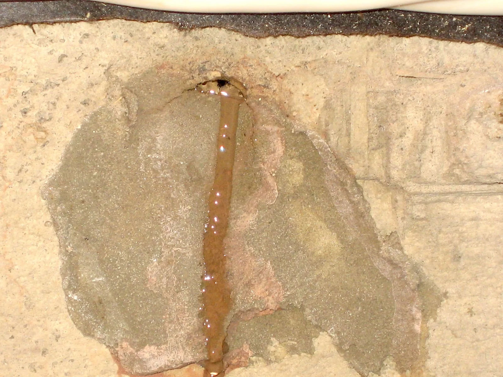 Actively leaking tie rod hole with muddy water running down a poured concrete foundation wall