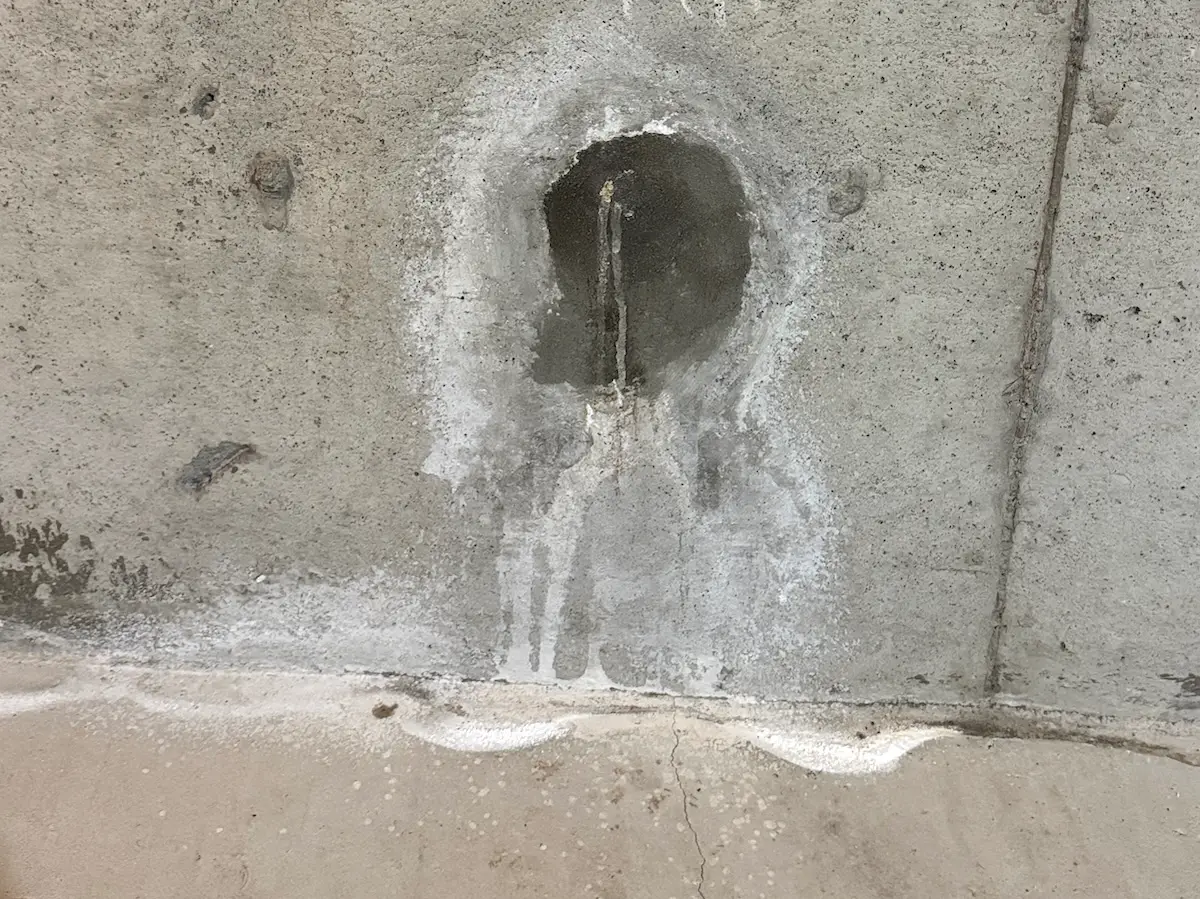 Tie rod hole with white efflorescence indicating repeated water infiltration